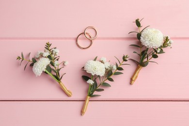 Photo of Small stylish boutonnieres and rings on pink wooden table, flat lay