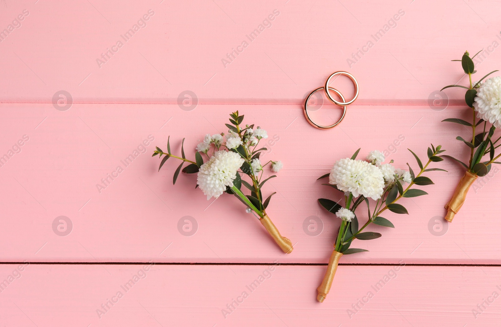 Photo of Small stylish boutonnieres and rings on pink wooden table, flat lay. Space for text