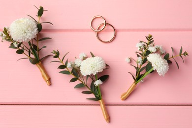 Photo of Small stylish boutonnieres and rings on pink wooden table, flat lay