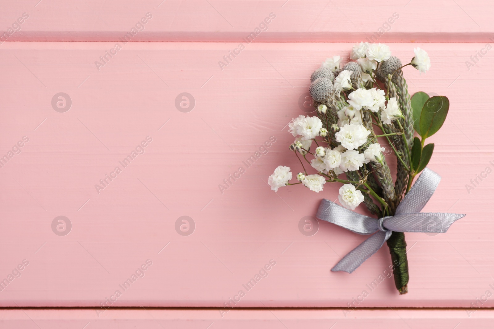 Photo of Small stylish boutonniere on pink wooden table, top view. Space for text