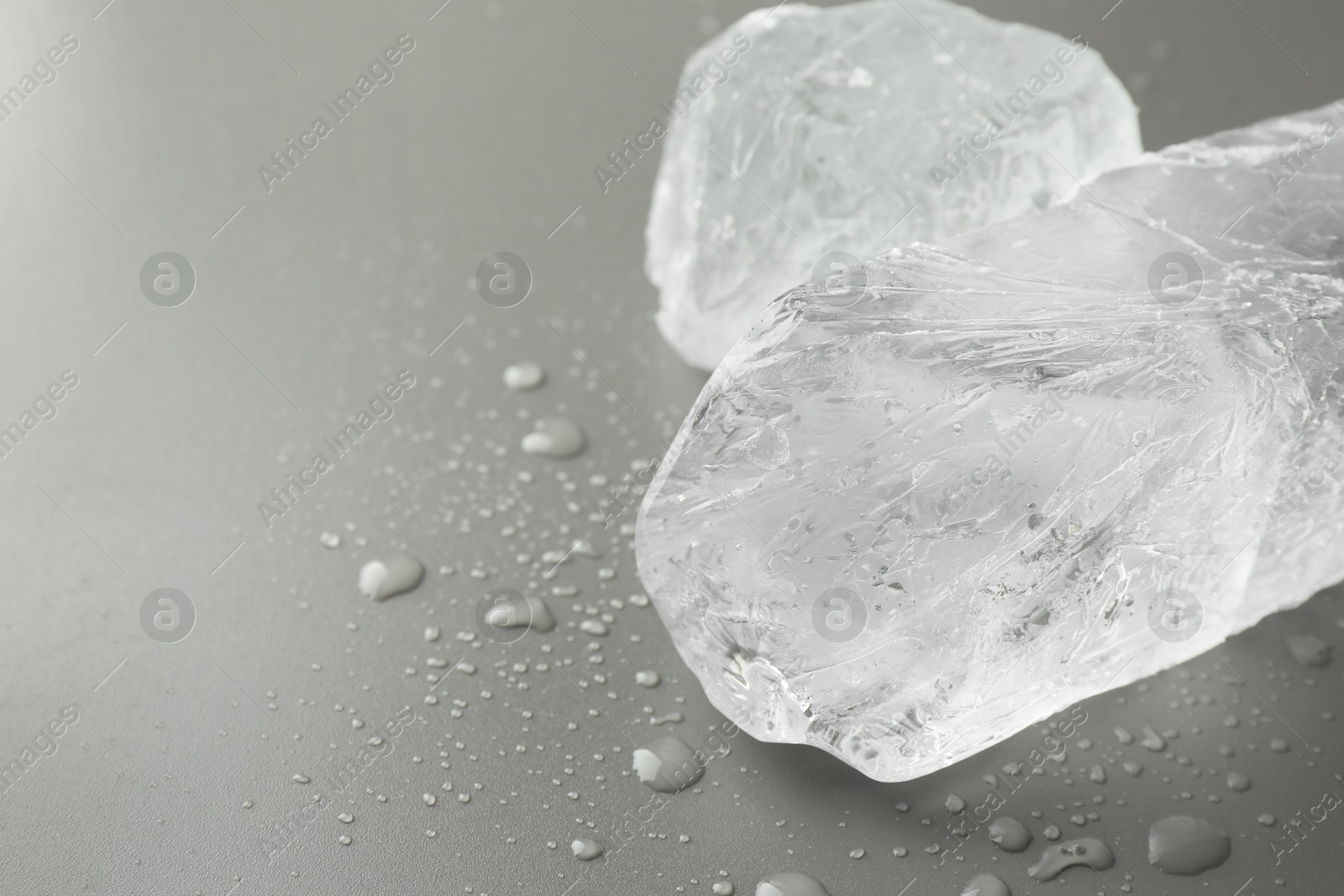 Photo of Pieces of clear ice and water drops on light grey table, closeup. Space for text