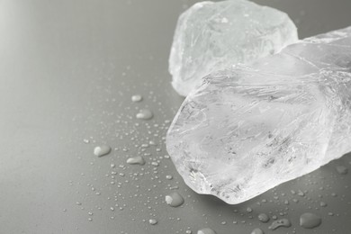 Pieces of clear ice and water drops on light grey table, closeup. Space for text