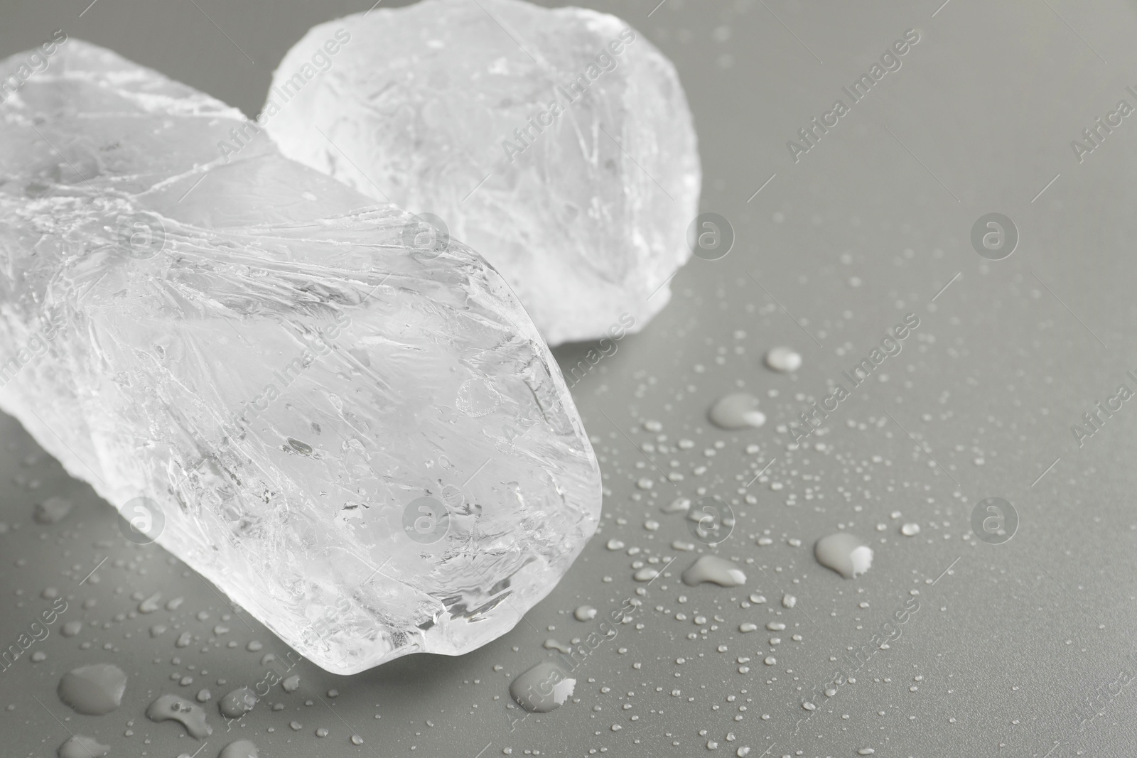 Photo of Pieces of clear ice and water drops on light grey table, closeup. Space for text