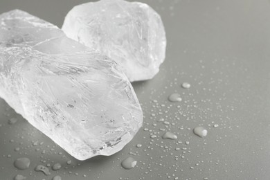 Pieces of clear ice and water drops on light grey table, closeup. Space for text