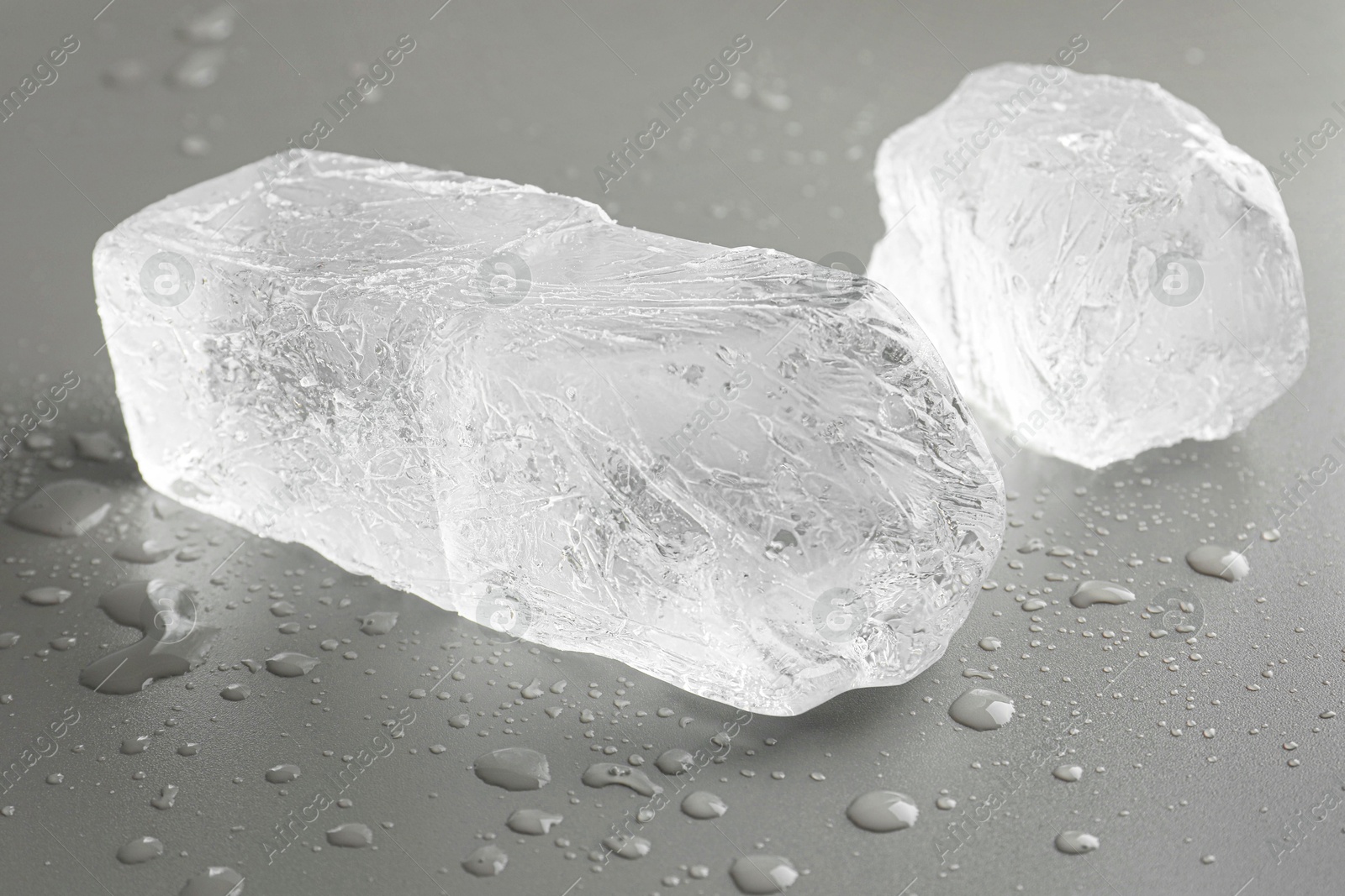 Photo of Pieces of clear ice and water drops on light grey table, closeup