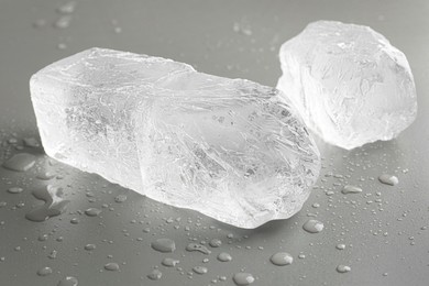 Pieces of clear ice and water drops on light grey table, closeup