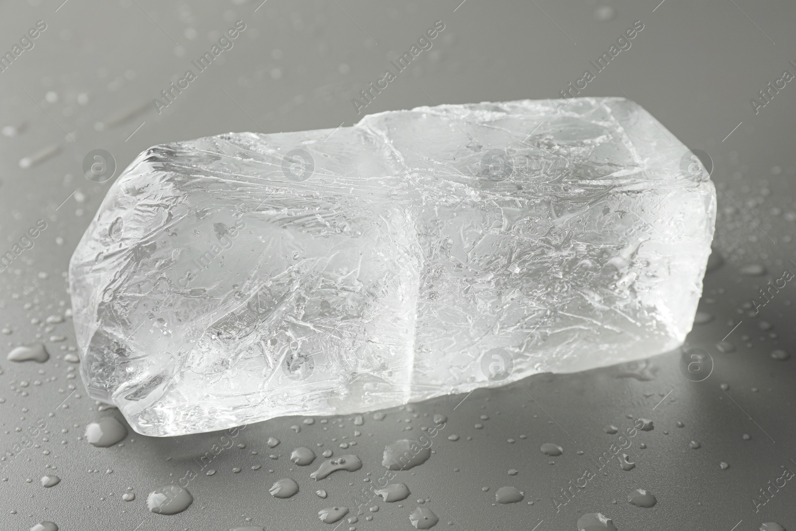 Photo of Piece of clear ice and water drops on light grey table, closeup