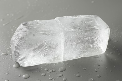 Piece of clear ice and water drops on light grey table, closeup