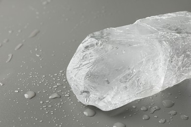 Photo of Piece of clear ice and water drops on light grey table, closeup