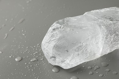 Piece of clear ice and water drops on light grey table, closeup