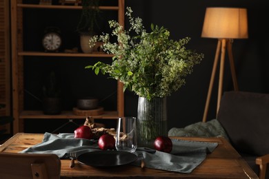 Photo of Set of clean dishware, ripe red apples and flowers on wooden table in stylish dining room