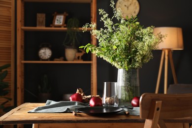 Set of clean dishware, ripe red apples and flowers on wooden table in stylish dining room