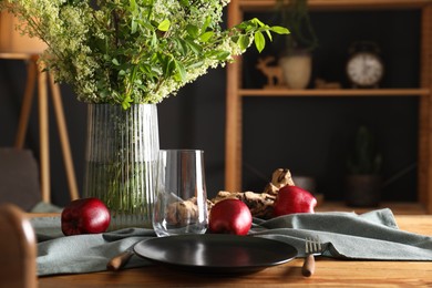 Photo of Set of clean dishware, ripe red apples and flowers on wooden table in stylish dining room