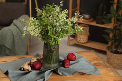 Ripe red apples and flowers on wooden table in stylish dining room