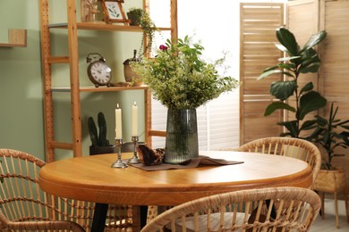 Photo of Vase with beautiful flowers and candles on wooden table in stylish dining room