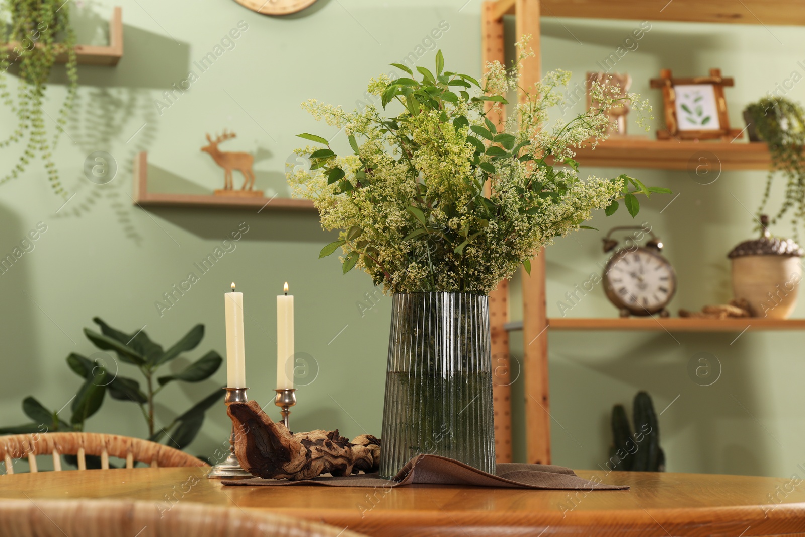 Photo of Vase with beautiful flowers and candles on wooden table in stylish dining room