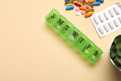 Different pills and organizer on beige background, flat lay. Space for text