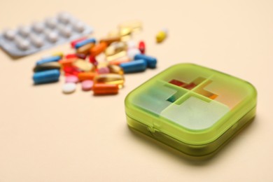 Photo of Organizer with different pills on beige background, closeup