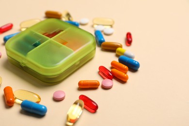 Different pills and organizer on beige background, closeup. Space for text