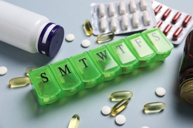 Different pills, organizer and medical jars on light background, closeup