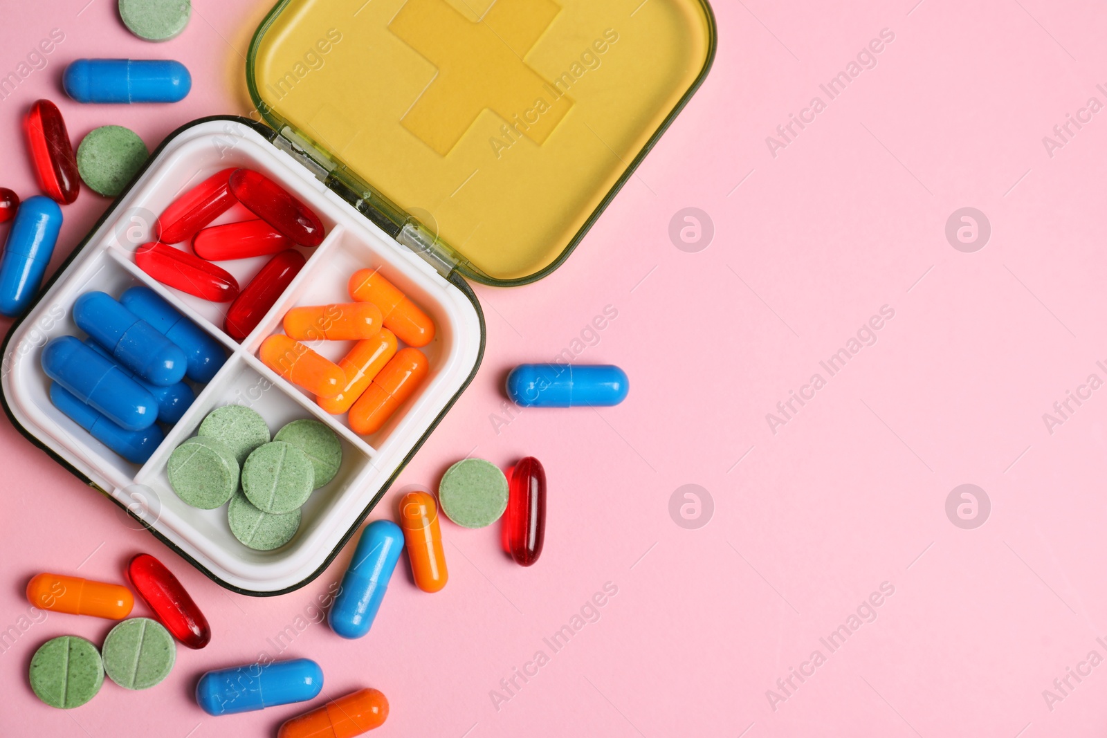 Photo of Different pills and organizer on pink background, flat lay. Space for text