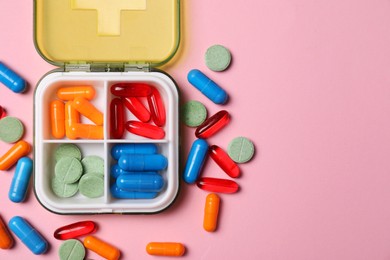 Photo of Different pills and organizer on pink background, flat lay. Space for text