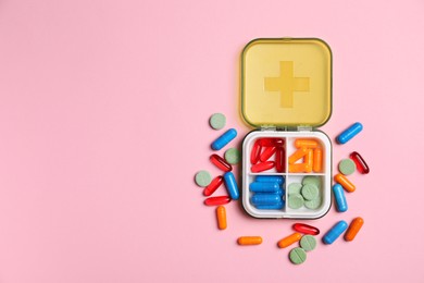 Photo of Different pills and organizer on pink background, flat lay. Space for text