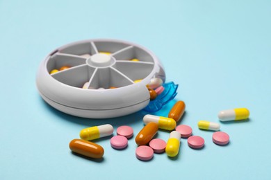 Photo of Different pills and organizer on light blue background, closeup