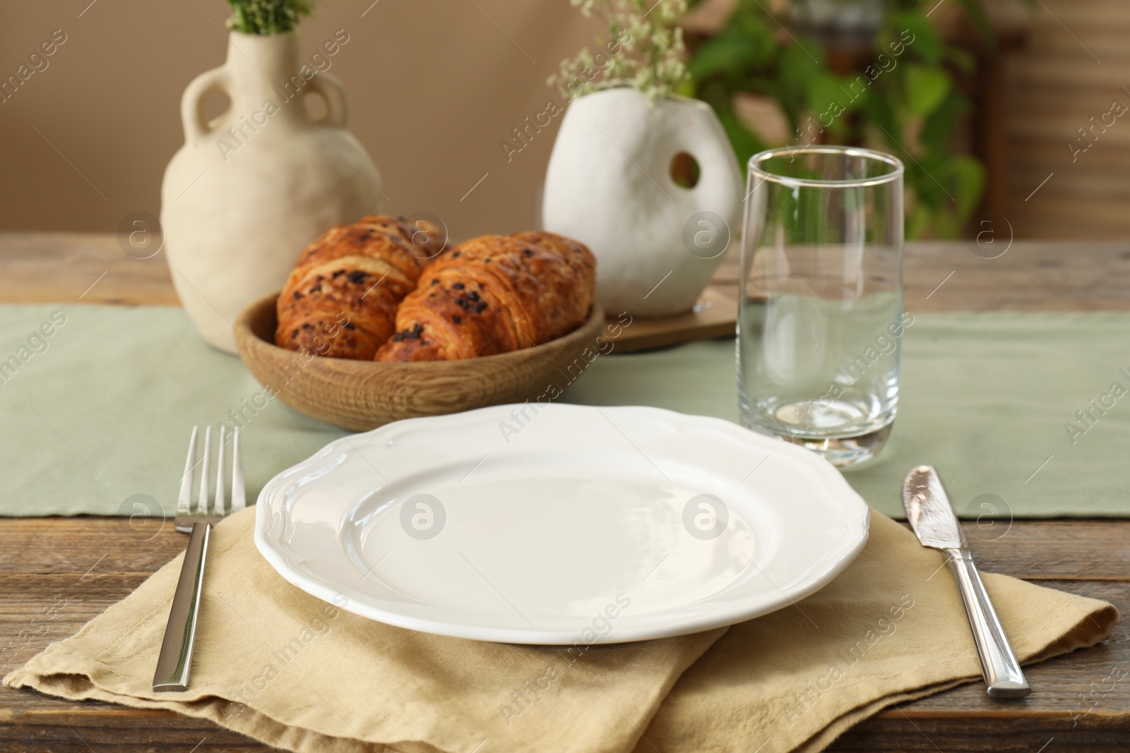 Photo of Clean tableware, flowers and fresh pastries on wooden table indoors