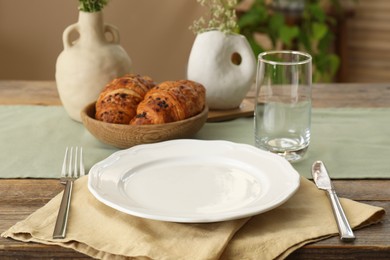 Clean tableware, flowers and fresh pastries on wooden table indoors