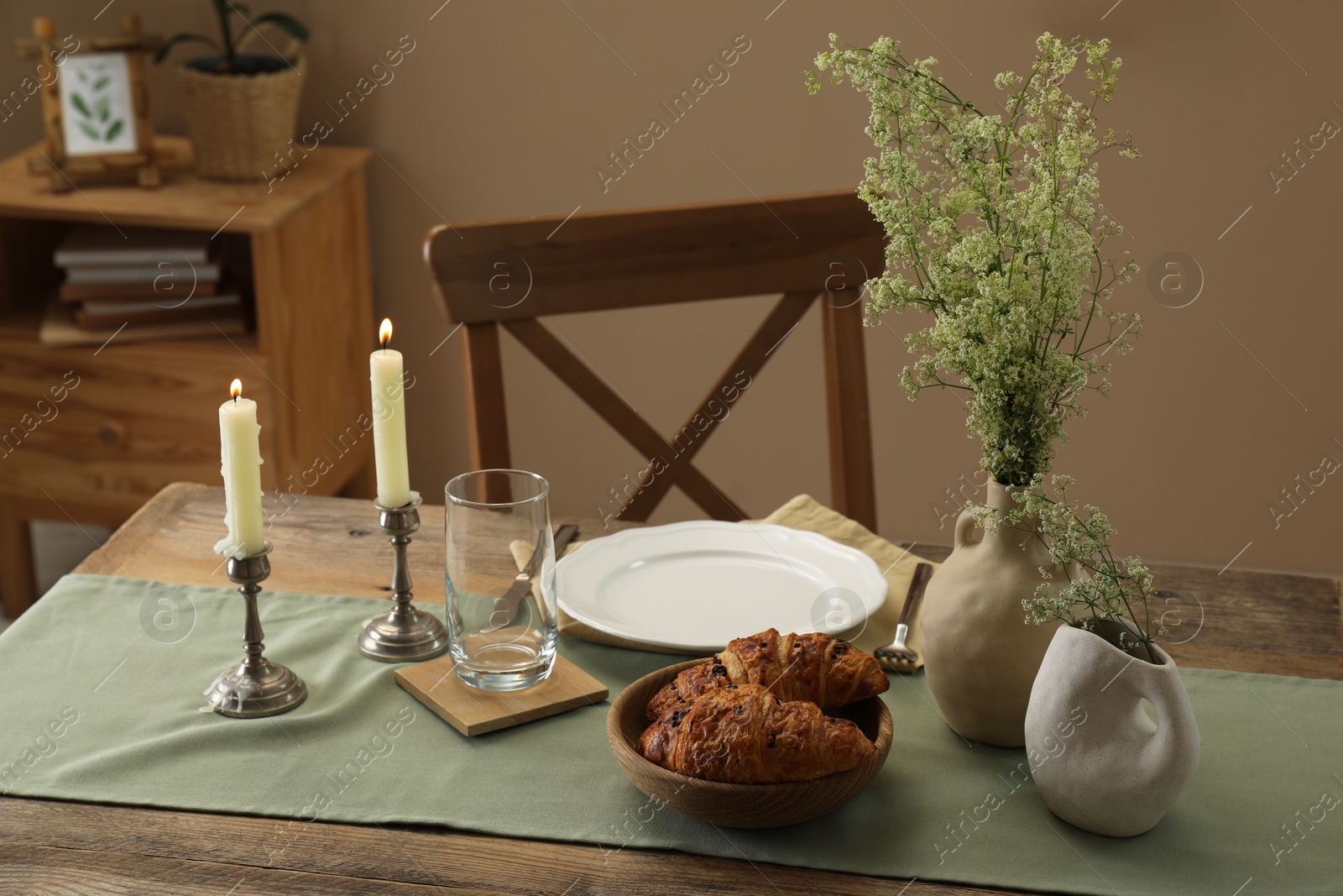 Photo of Clean tableware, candlesticks, flowers and fresh pastries on wooden table indoors