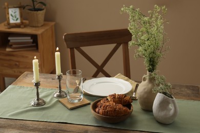 Clean tableware, candlesticks, flowers and fresh pastries on wooden table indoors