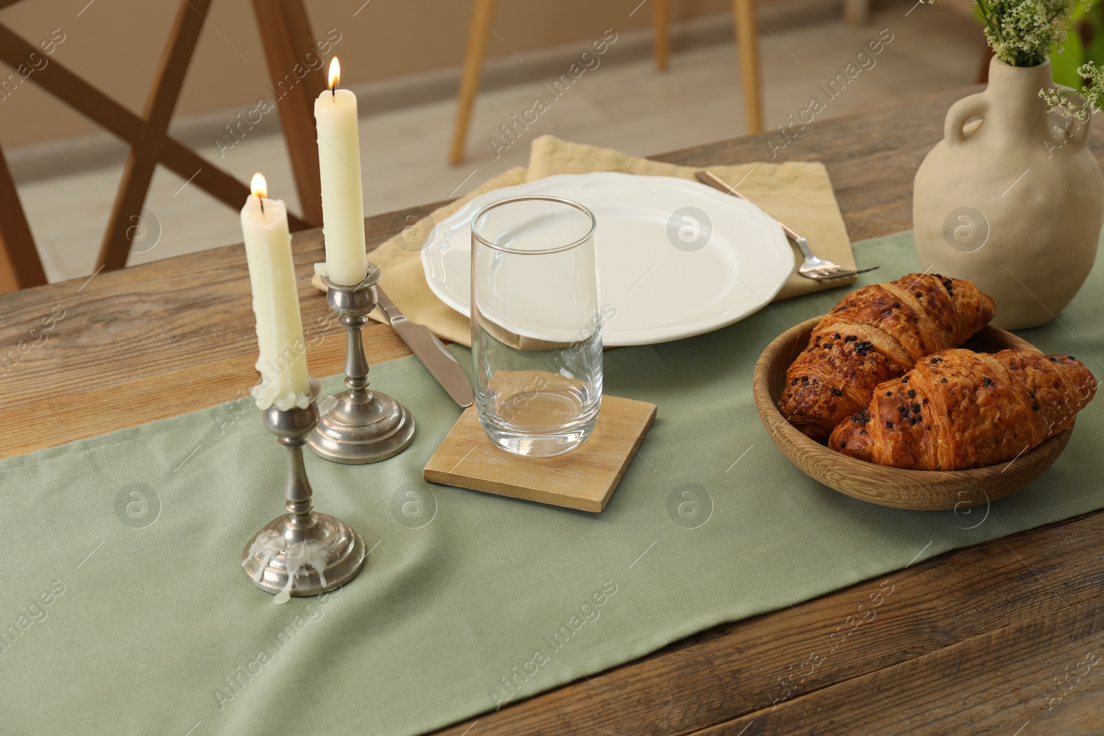 Photo of Clean tableware, candlesticks, flowers and fresh pastries on wooden table indoors