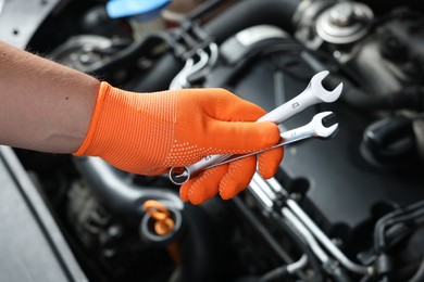 Photo of Auto mechanic with ratcheting wrenches fixing car at automobile repair shop, closeup