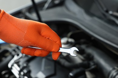 Auto mechanic with ratcheting wrench fixing car at automobile repair shop, closeup