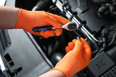 Auto mechanic with torque wrench fixing car at automobile repair shop, closeup