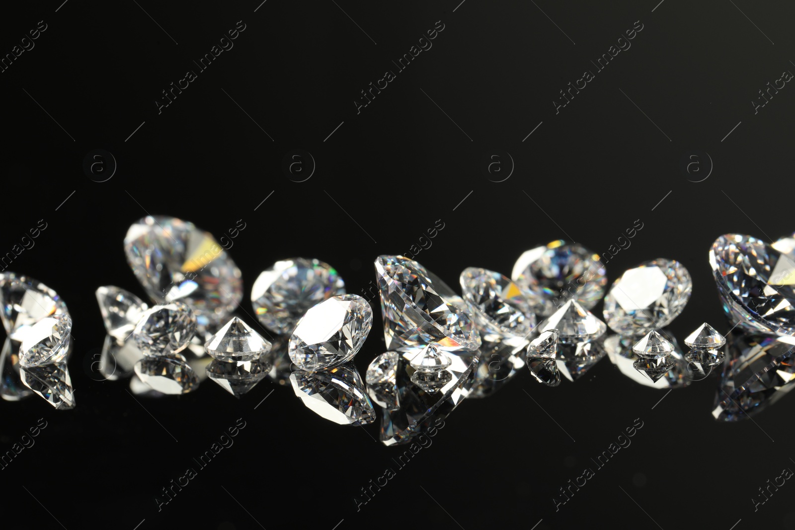 Photo of Many beautiful shiny diamonds on black mirror surface, closeup