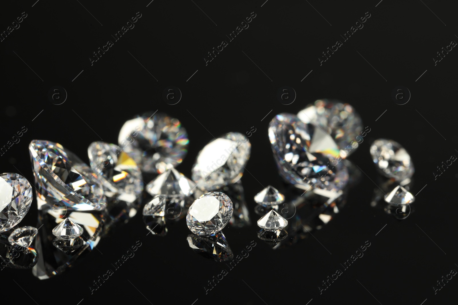 Photo of Many beautiful shiny diamonds on black mirror surface, closeup