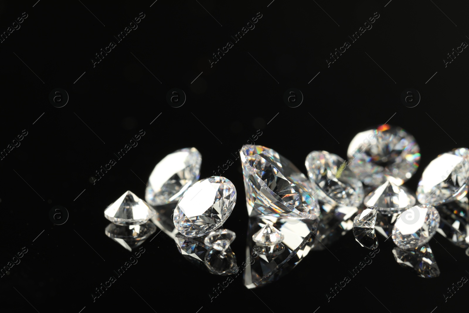 Photo of Many beautiful shiny diamonds on black mirror surface, closeup