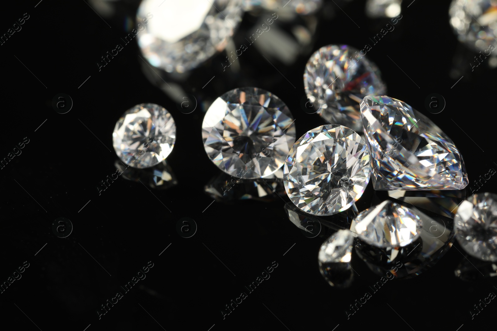 Photo of Many beautiful shiny diamonds on black mirror surface, closeup