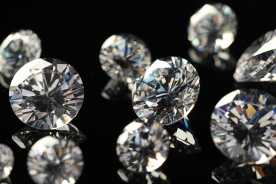 Photo of Many beautiful shiny diamonds on black mirror surface, closeup