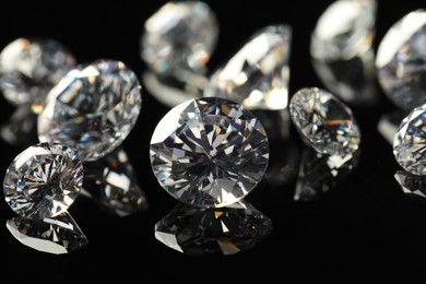 Photo of Many beautiful shiny diamonds on black mirror surface, closeup