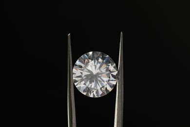 Tweezers with beautiful shiny diamond on black background, closeup