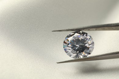 Photo of Tweezers with beautiful shiny diamond on white fabric, closeup. Space for text