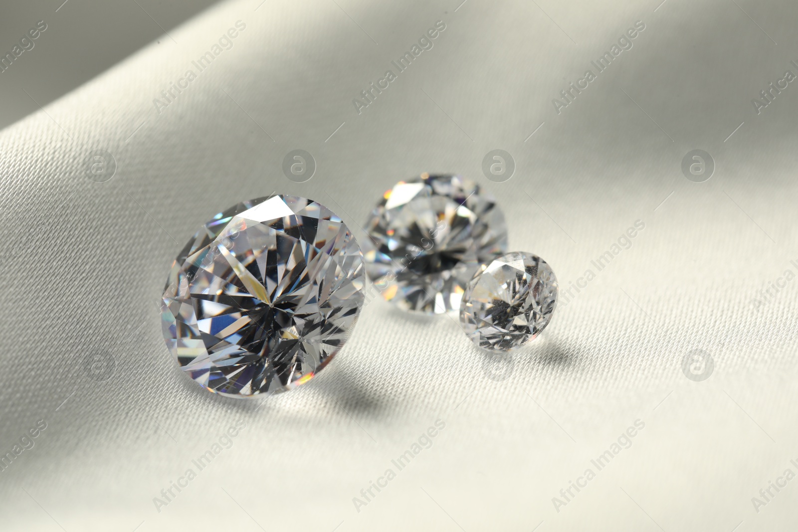 Photo of Three beautiful shiny diamonds on white fabric, closeup