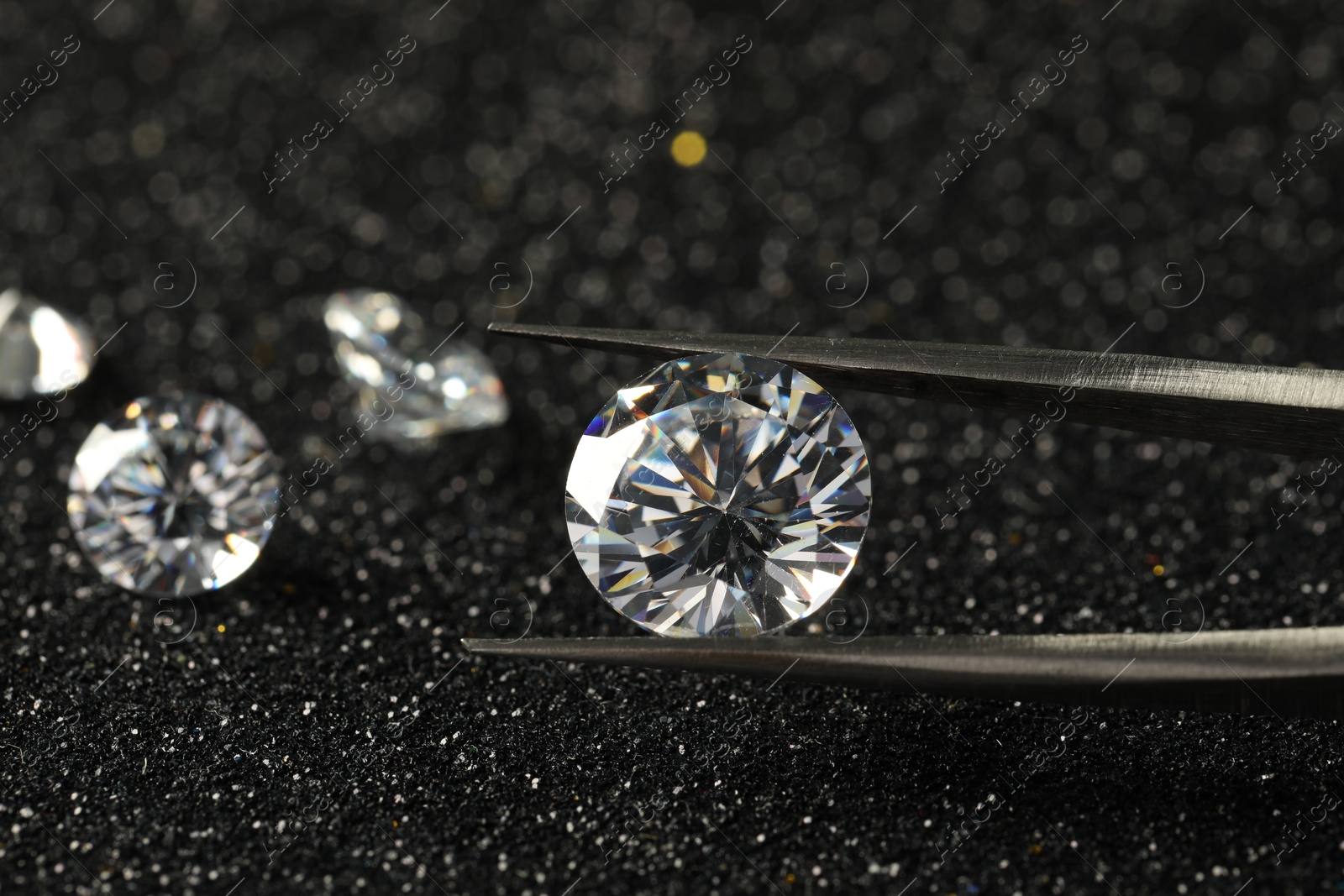 Photo of Tweezers with beautiful diamond on dark shiny background, closeup