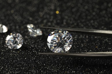 Tweezers with beautiful diamond on dark shiny background, closeup