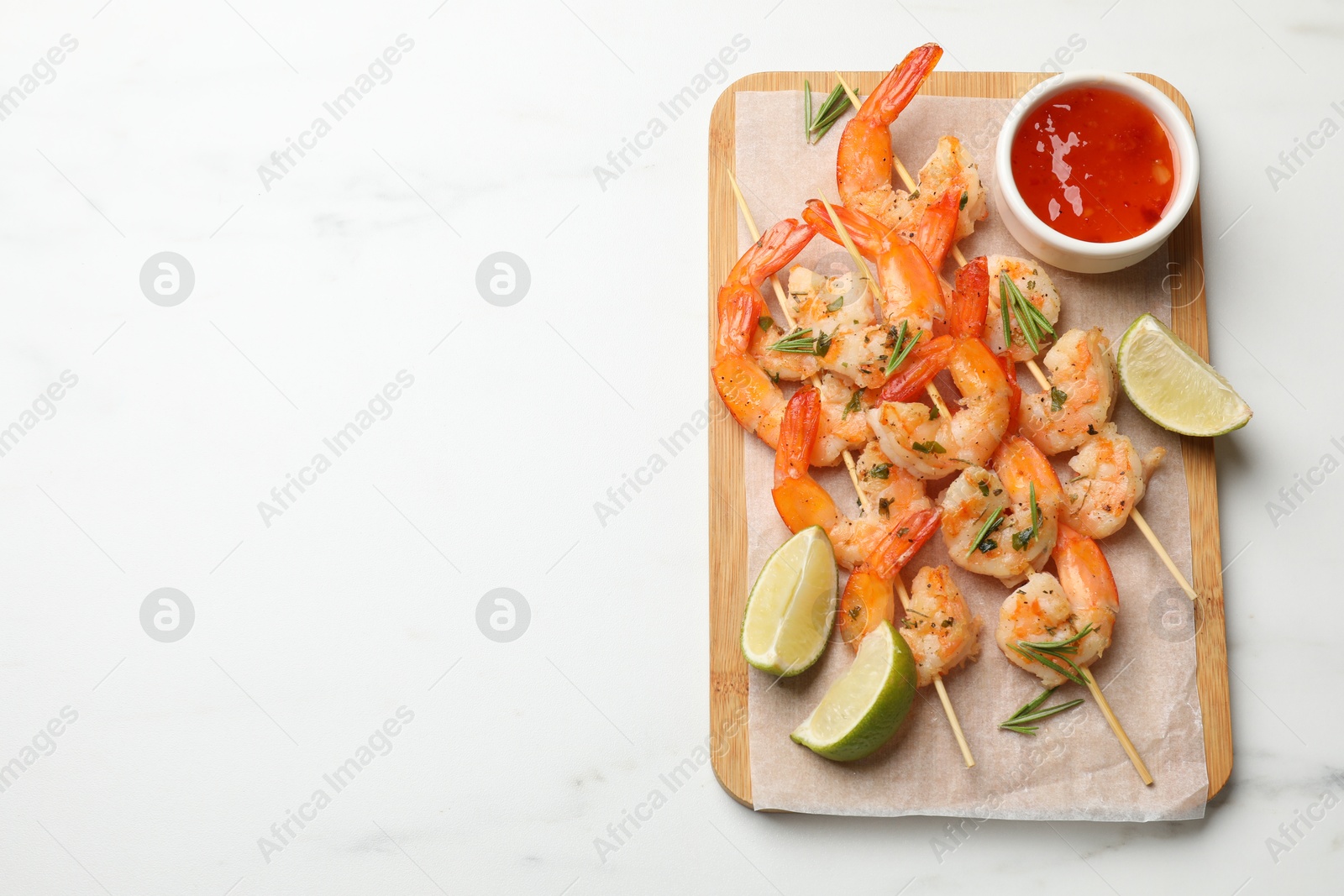 Photo of Skewers with delicious grilled shrimps served on white table, top view. Space for text