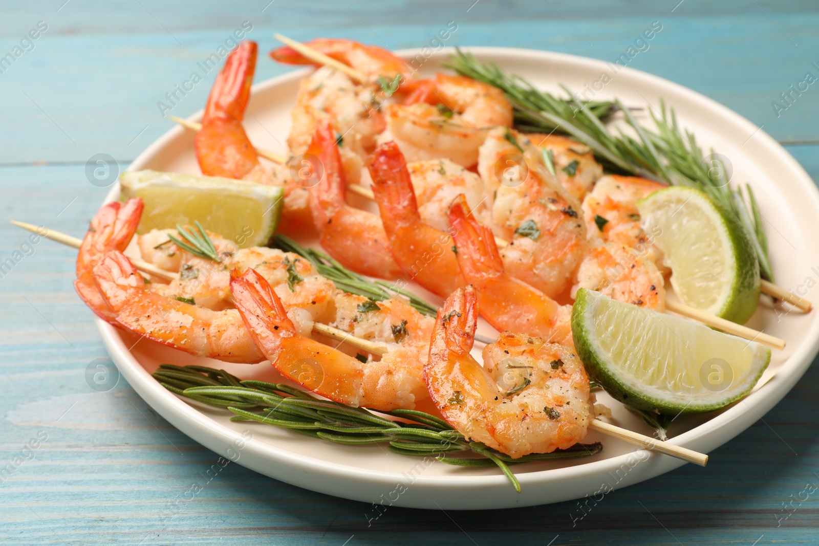 Photo of Skewers with delicious grilled shrimps served on blue wooden table, closeup