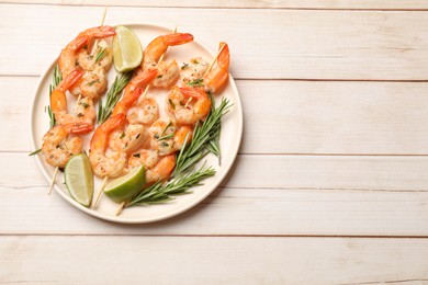 Photo of Skewers with delicious grilled shrimps served on white wooden table, top view. Space for text